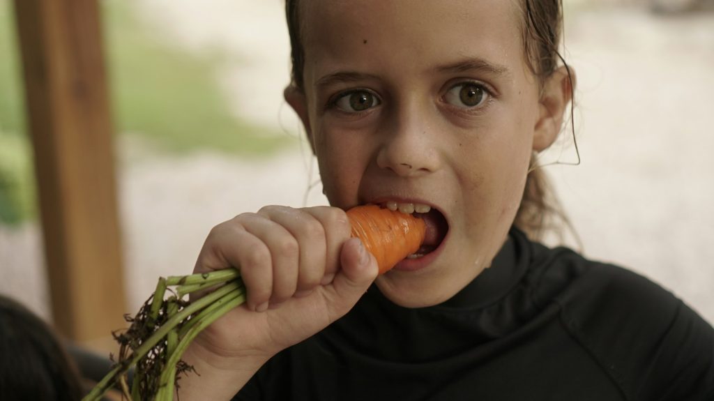 Girl biting into a fresh carrot